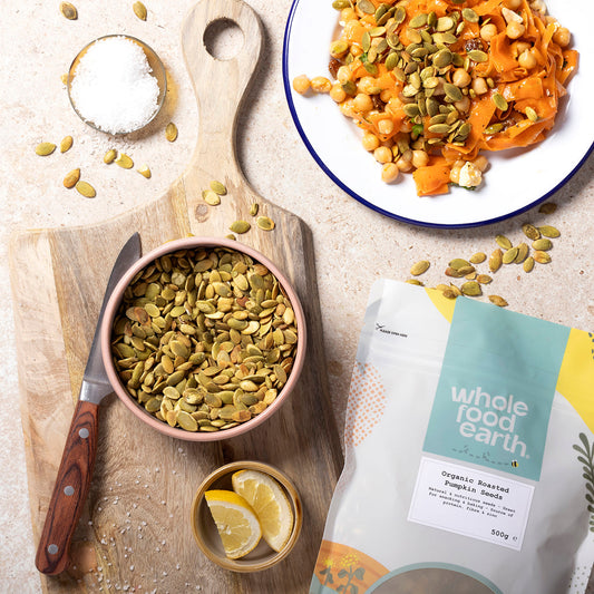 Organic roasted pumpkin seeds from Whole Food Earth, displayed in a bowl with some seeds scattered on a wooden surface.