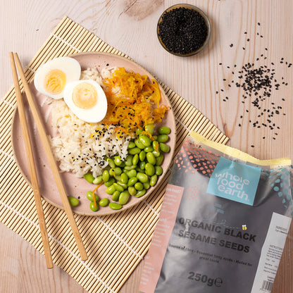 Black organic sesame seeds from Whole Food Earth in a clear glass bowl, close-up view of small, shiny seeds on a wooden surface.