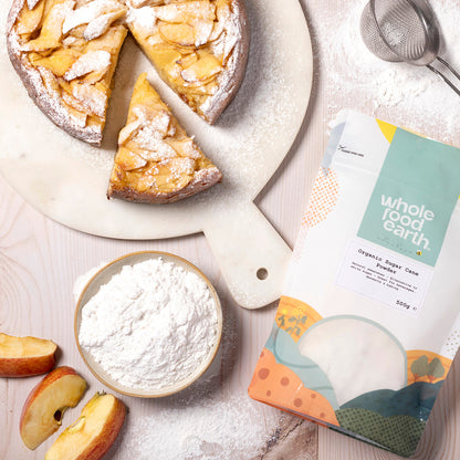 Organic sugar cane powder from Whole Food Earth, displayed on a wooden table with a spoon and fresh ingredients for natural sweetness.