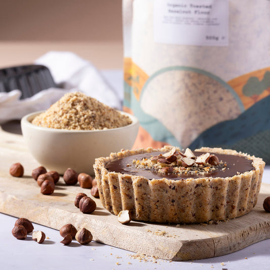 Organic toasted hazelnut flour from Whole Food Earth, shown in a natural setting with baking ingredients and a wooden spoon.