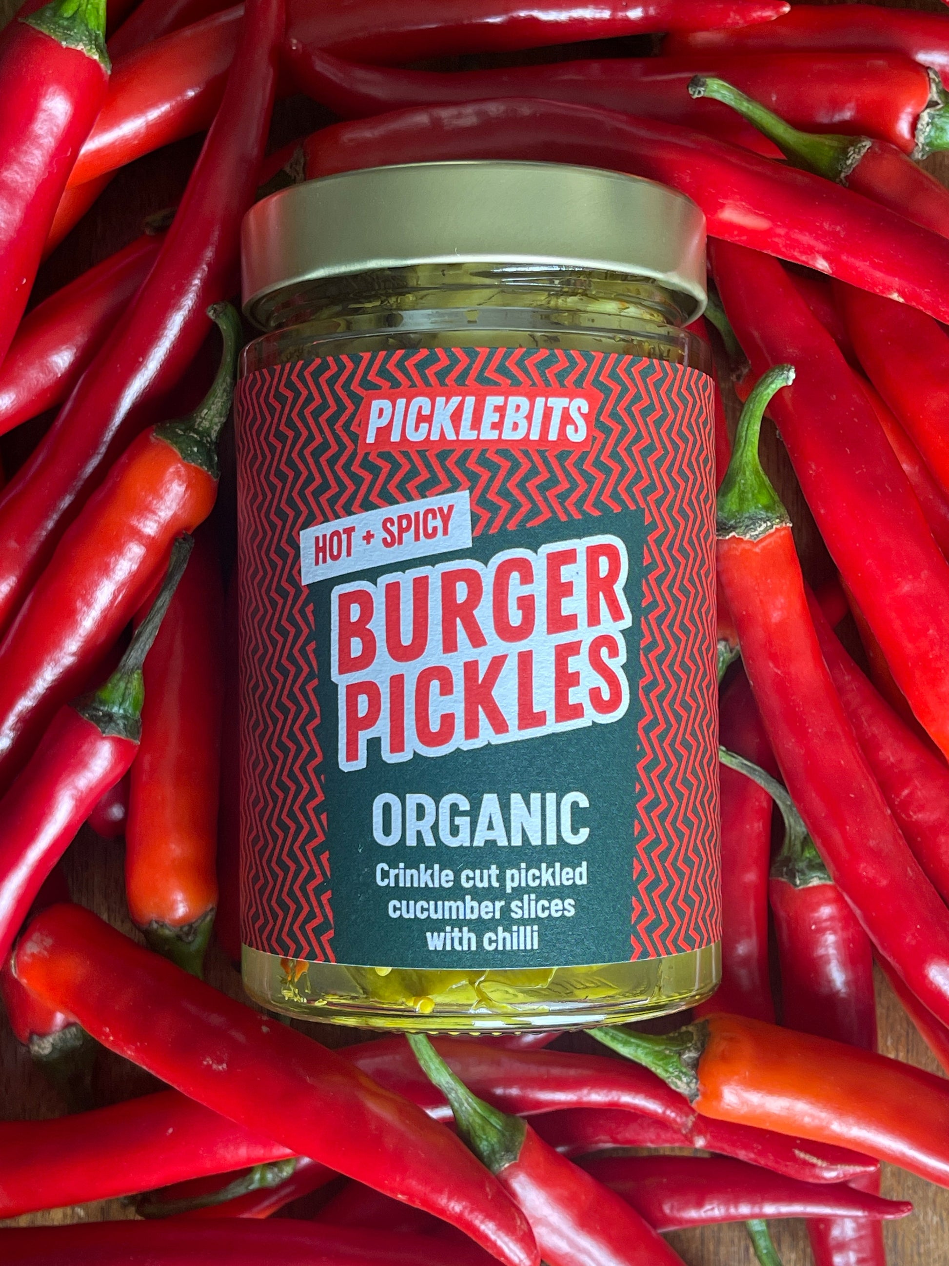 Organic spicy burger pickles by PICKLEBITS in a jar, showcasing vibrant green pickles with hot and spicy seasoning.