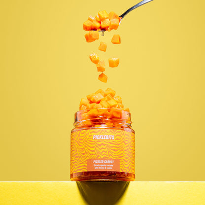 Jar of organic pickled carrot chopped tumbling on yellow background