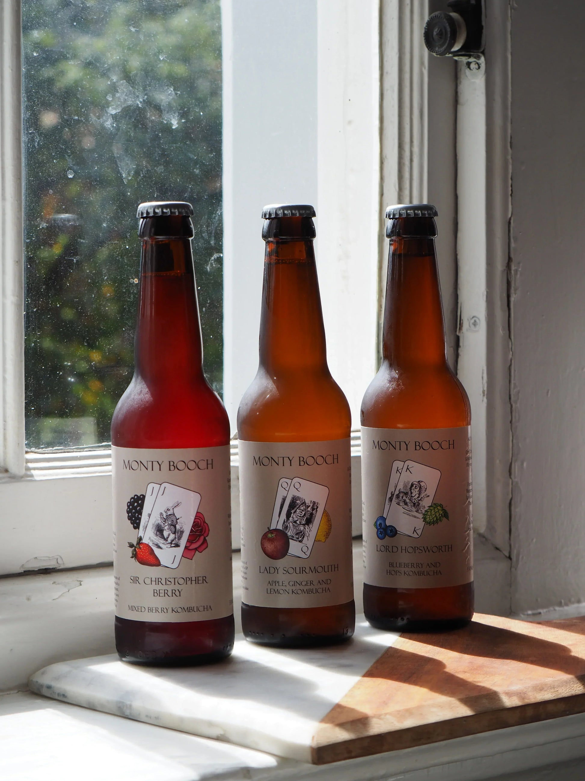 Monty Booch Lord Hopsworth Hopped Blueberry Kombucha 12-pack of 330ml bottles on a table with blueberries and hops.