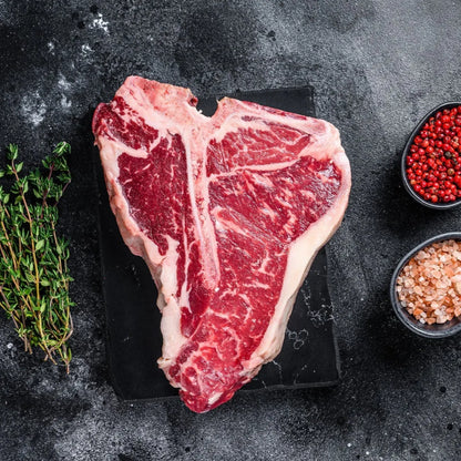 Primrose Herd dry-aged beef T-bone steak on cutting board, showcasing marbled meat and bone with rustic presentation.