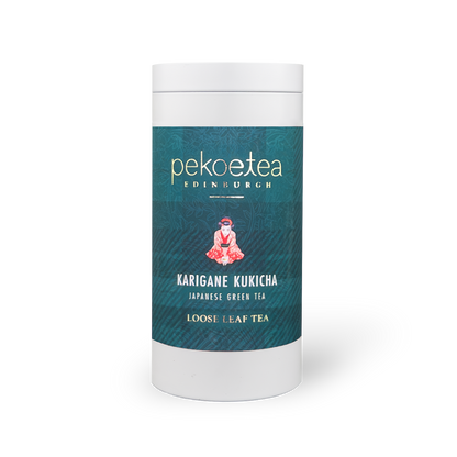 Jar of PekoeTea Edinburgh Karigane Kukicha green tea leaves in a caddy, showcasing the tea's light-colored twig and leaf blend.