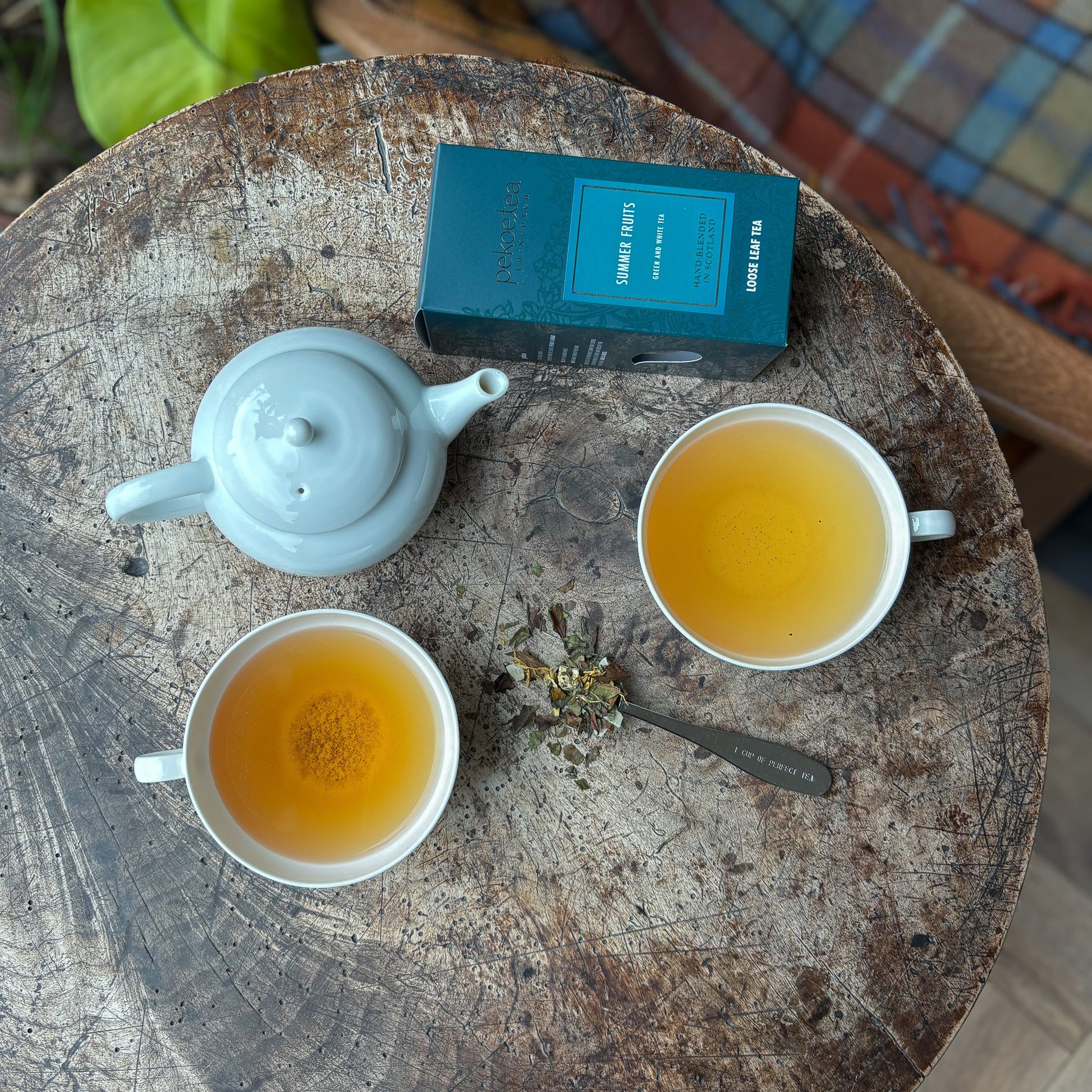 A cup of PekoeTea Edinburgh Summer Fruits tea with fresh summer fruits and tea leaves in a bright, inviting setting