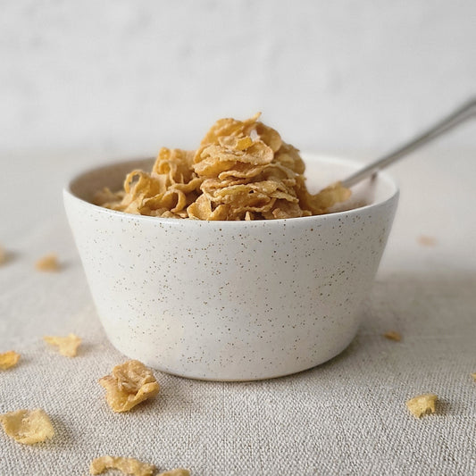 White ceramic breakfast bowl with "Pepper White" design by Katie L Thompson Designs, filled with cornflakes and a spoon.