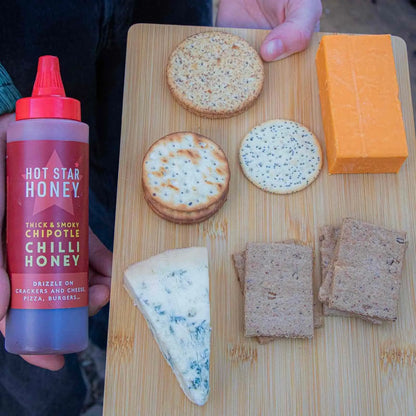 Hot Star Honey Chipotle Chilli Honey drizzled on cheese and crackers, showcasing its spicy, sweet flavor and vibrant amber color.