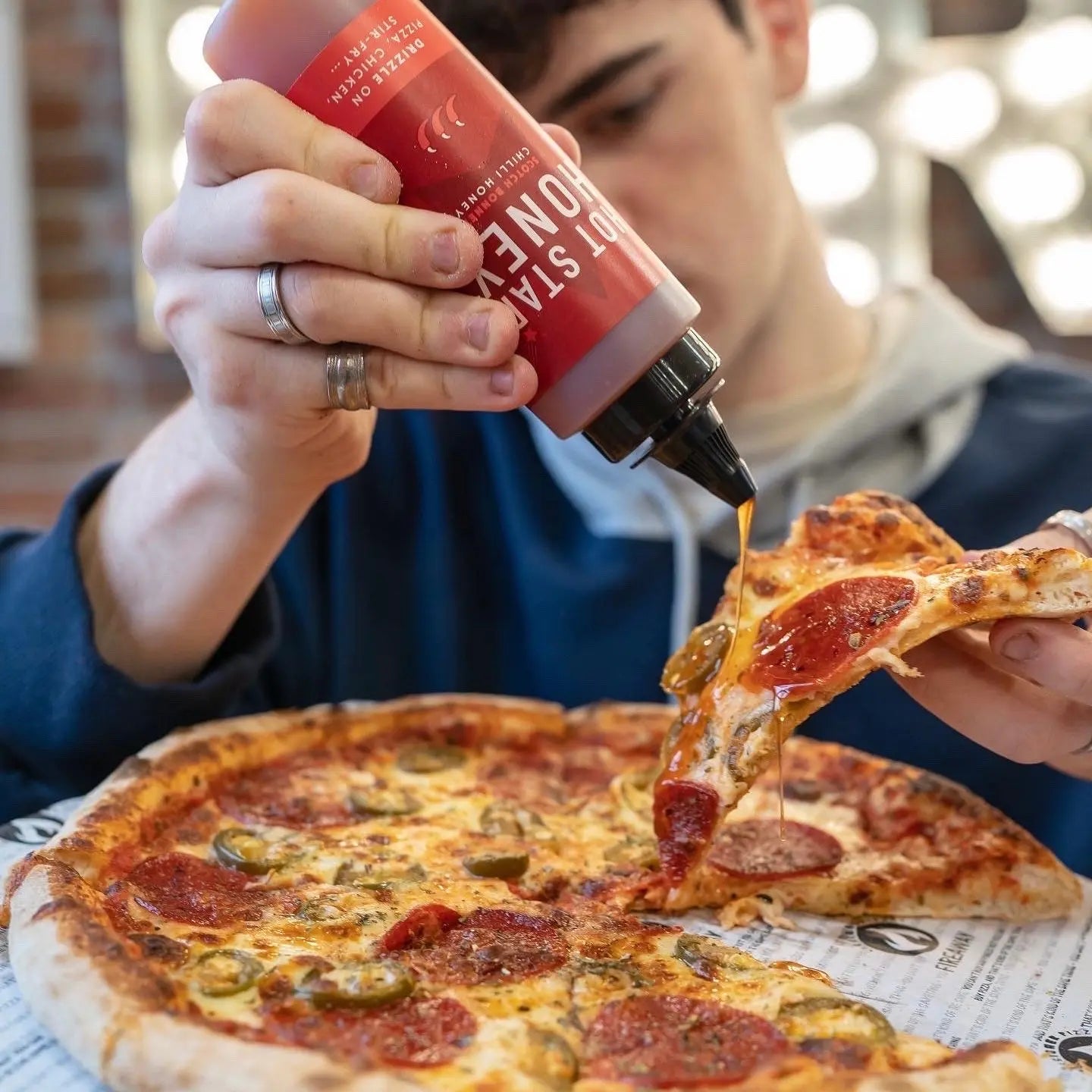 Scotch Bonnet chili honey from Hot Star Honey drizzled on a pizza, showcasing the spicy, sweet condiment's vibrant appearance.