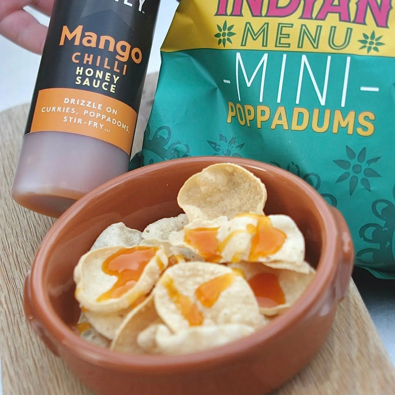 Asian-inspired Mango Chilli Honey Sauce from Hot Star Honey served on crispy popadoms with mango slices and chili peppers.