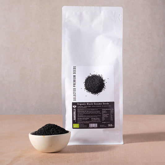 Organic black sesame seeds in a clear container, showcasing small black seeds from RAWGORILLA brand on a white background.