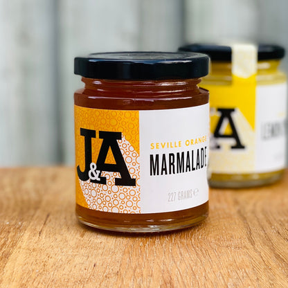 Janda Seville Orange Marmalade jar with slices of Seville oranges and a spoon on a rustic wooden surface.