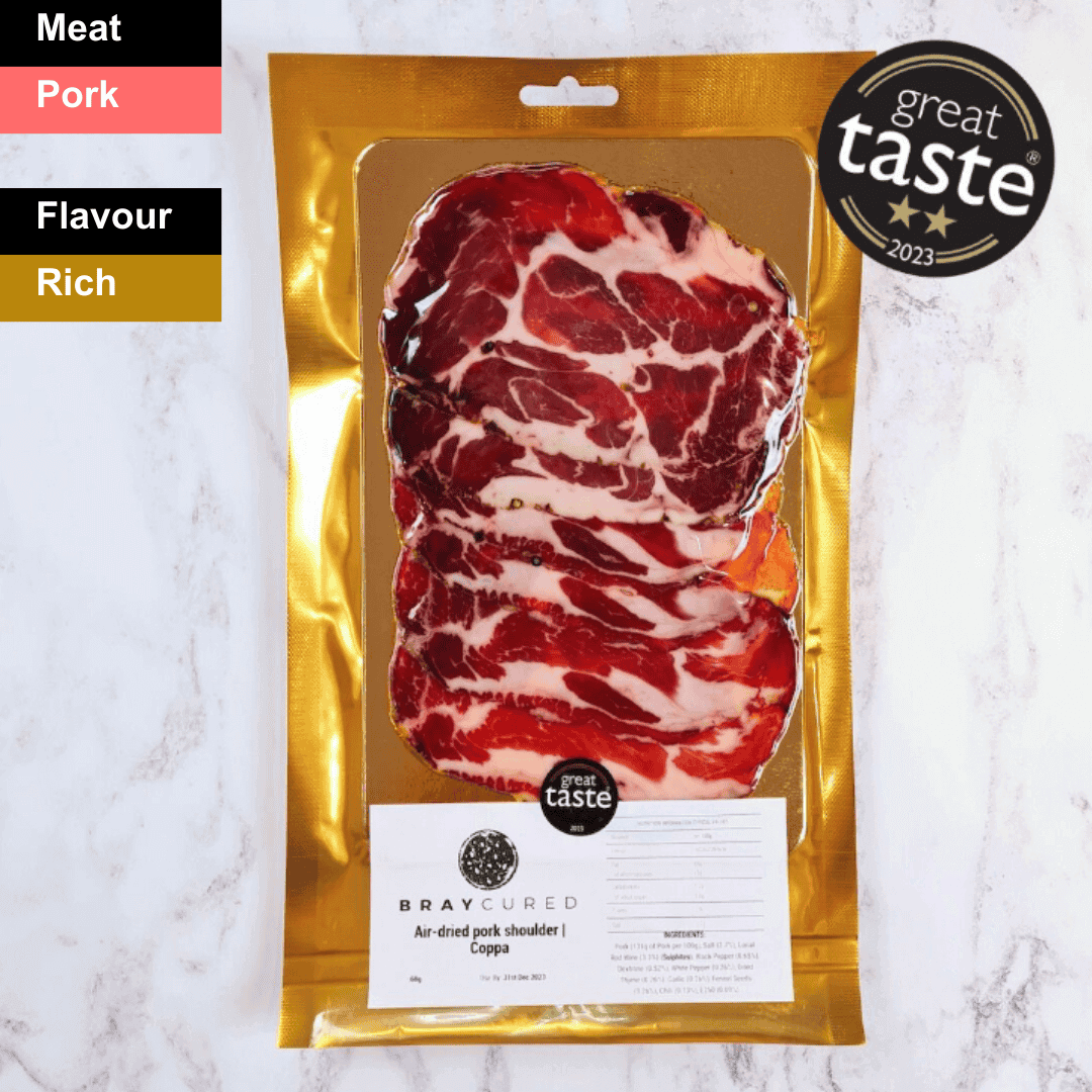 Slices of Bray Cured air-dried Coppa, a spicy charcuterie meat with marbled red and white fat, arranged on a wooden board.