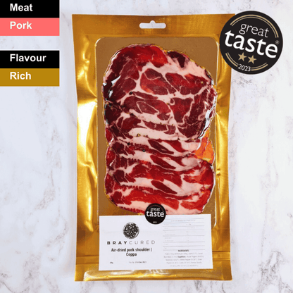 Slices of Bray Cured air-dried Coppa, a spicy charcuterie meat with marbled red and white fat, arranged on a wooden board.