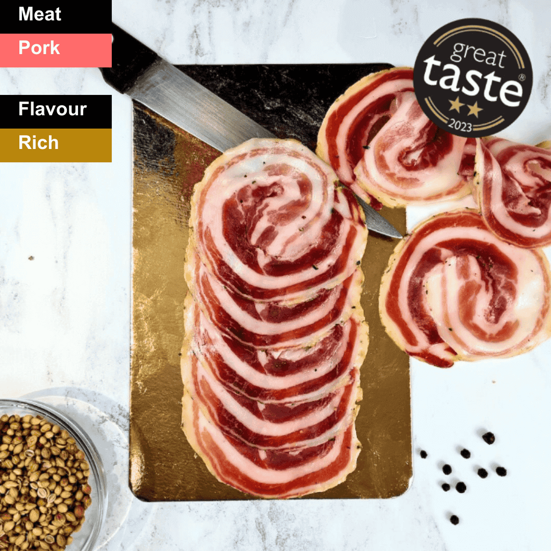 Thin slices of Bray Cured spicy pancetta, a flavorful charcuterie meat with a rich, marbled appearance on a wooden board.