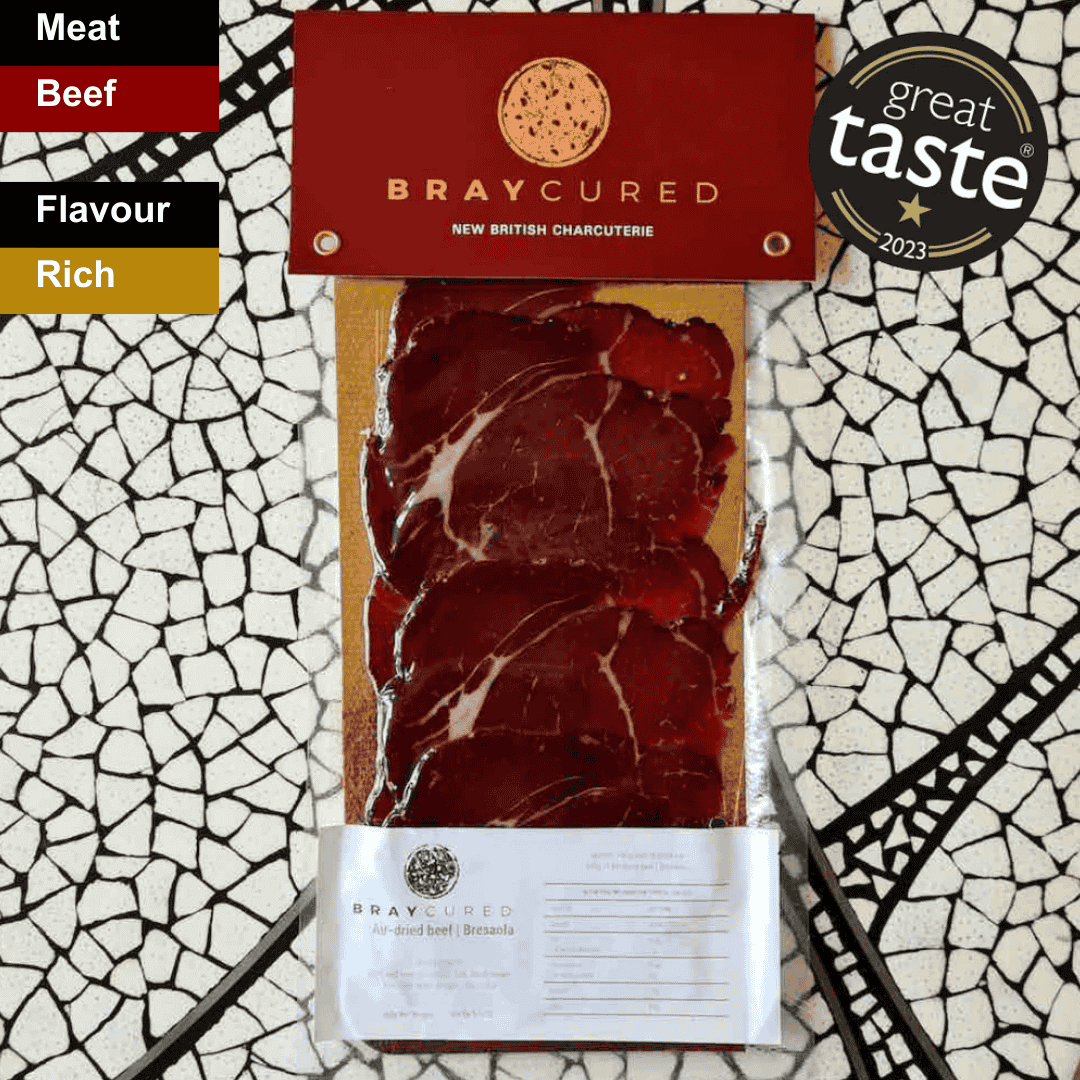 Thin slices of Bray Cured Classic Bresaola charcuterie with a spicy seasoning, displayed on a wooden serving board.
