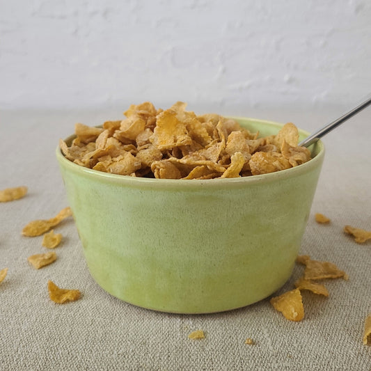 Spring green breakfast bowl by Katie L Thompson Designs filled with cereal and a spoon, showcasing a vibrant, modern ceramic design.