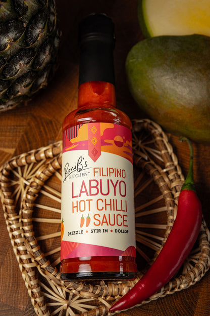Filipino Style Labuyo Hot Chilli Sauce by RoniBs Kitchen in a glass bottle with a red chili label on a wooden surface.