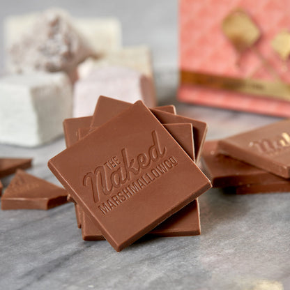 Naked marshmallow surrounded by milk chocolate thin candies from THE MARSHMALLOW FACTORY, showcasing the smooth chocolate coating.