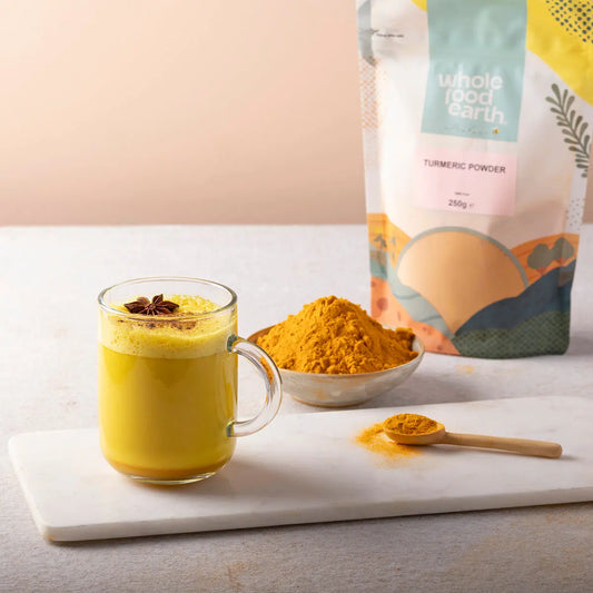 Organic turmeric powder from Whole Food Earth displayed in a jar with turmeric root and spice on a rustic wooden surface.