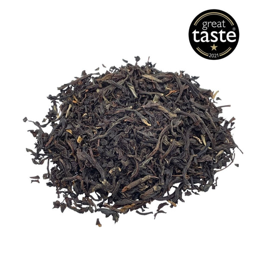 Loose leaf English Breakfast tea by Camellios with dark tea leaves and a rustic tea tin in the background.