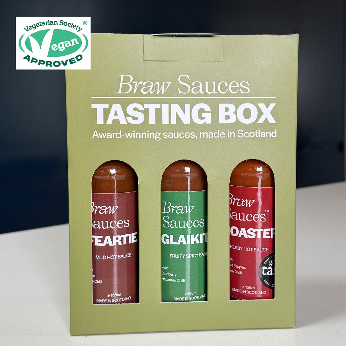 Vegan Tasting Box Sauces Gift Set by Braw Sauces featuring an assortment of colorful, bottled vegan sauces on a wooden surface.