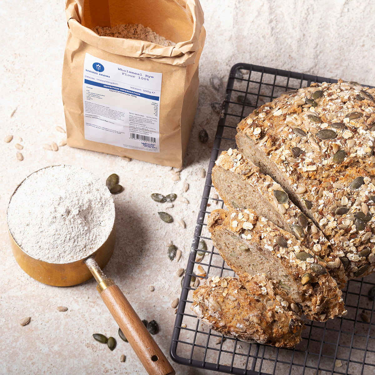 Wholemeal rye flour in a bag from Whole Food Earth on a rustic wooden surface, with a spoon and grains nearby.