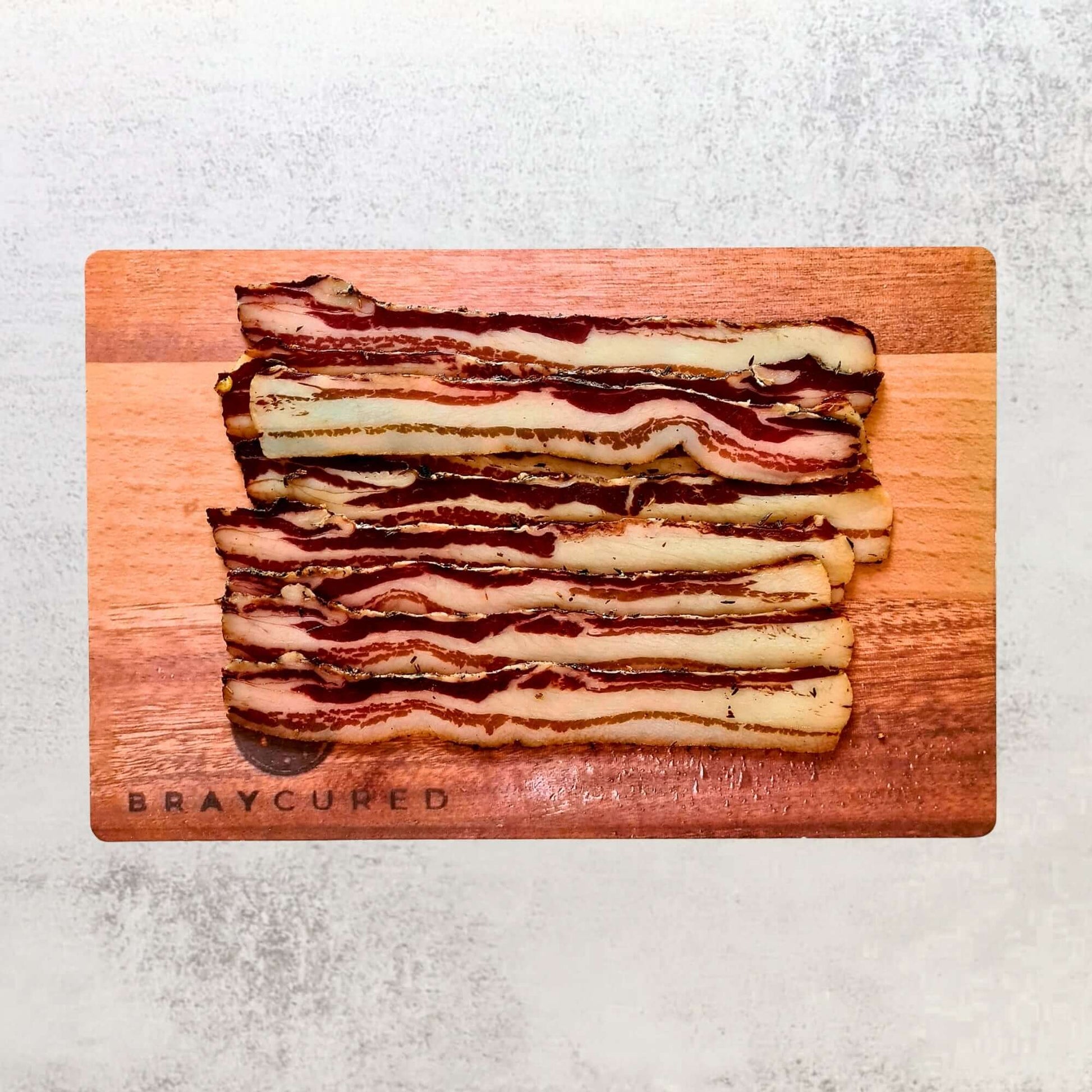 Thinly sliced Bray Cured pancetta, air-dried charcuterie meat on a serving board, showcasing its marbled texture and rich flavor.