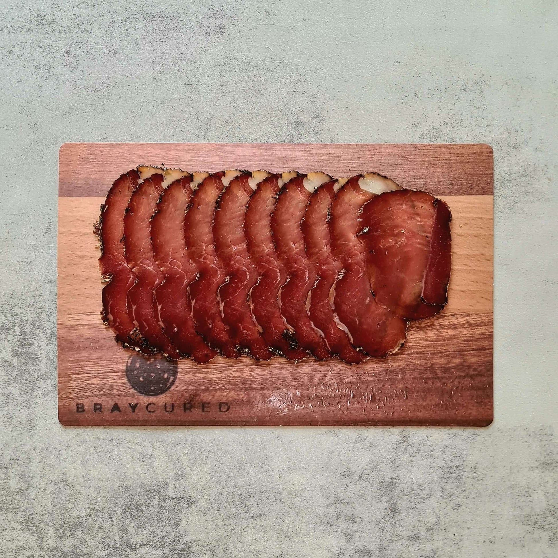 Thin slices of Bray Cured air-dried ham on a wooden board, showcasing the rich marbling and artisanal charcuterie presentation.