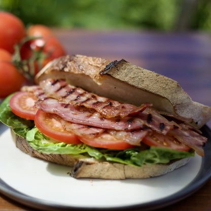 Sliced smoked back bacon from Primrose Herd, dry cured, displayed in a bacon bap sandwich with fresh bread and toppings.