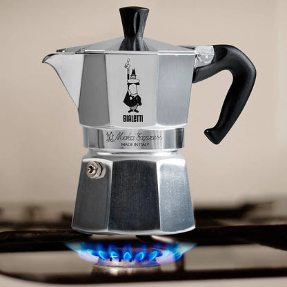Bialetti Moka Express stovetop espresso maker on a gas cooker, showcasing its classic aluminum design and handle.