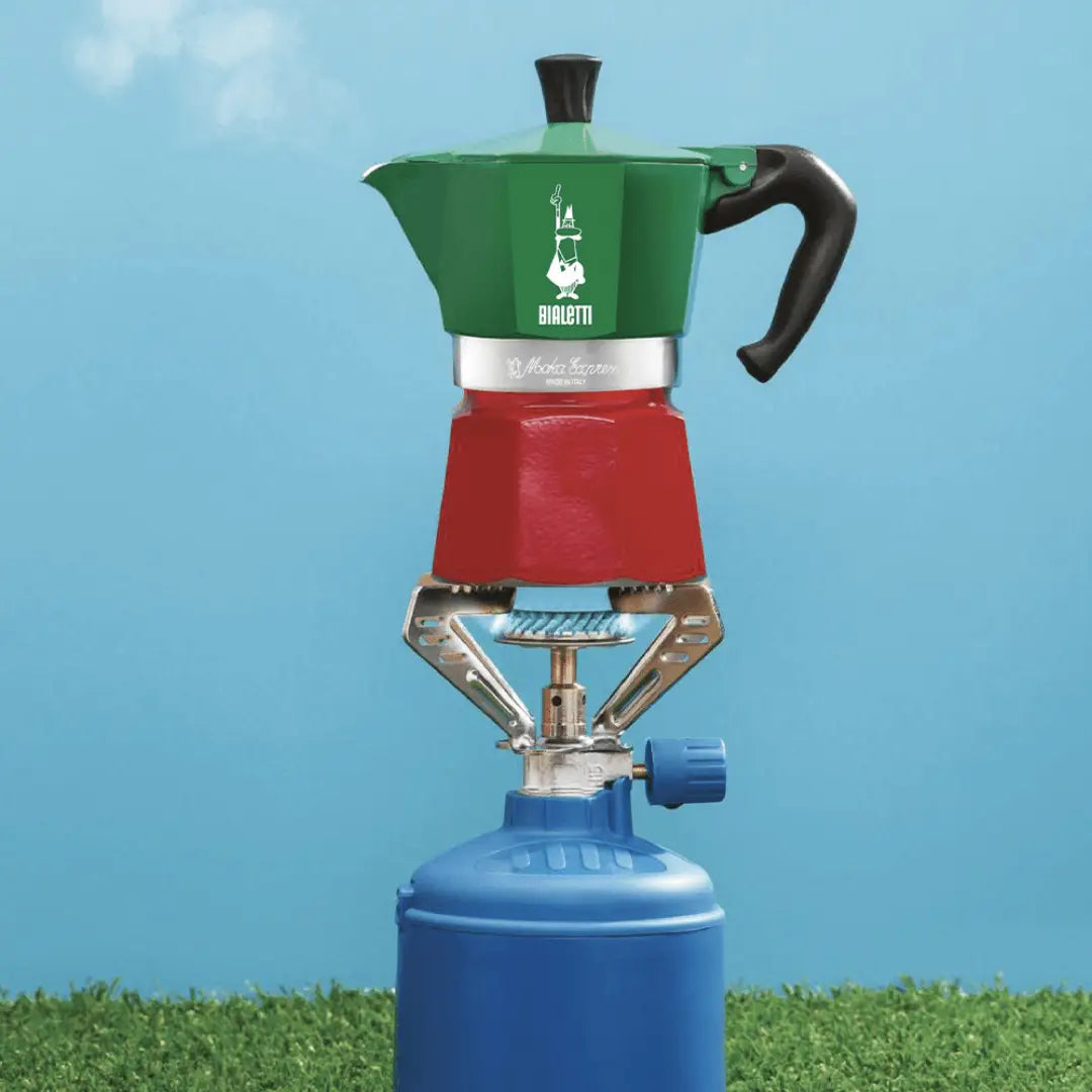 Bialetti Moka Express Tricolore Italia stovetop coffee maker in stainless steel with colorful accents, outdoor setting.