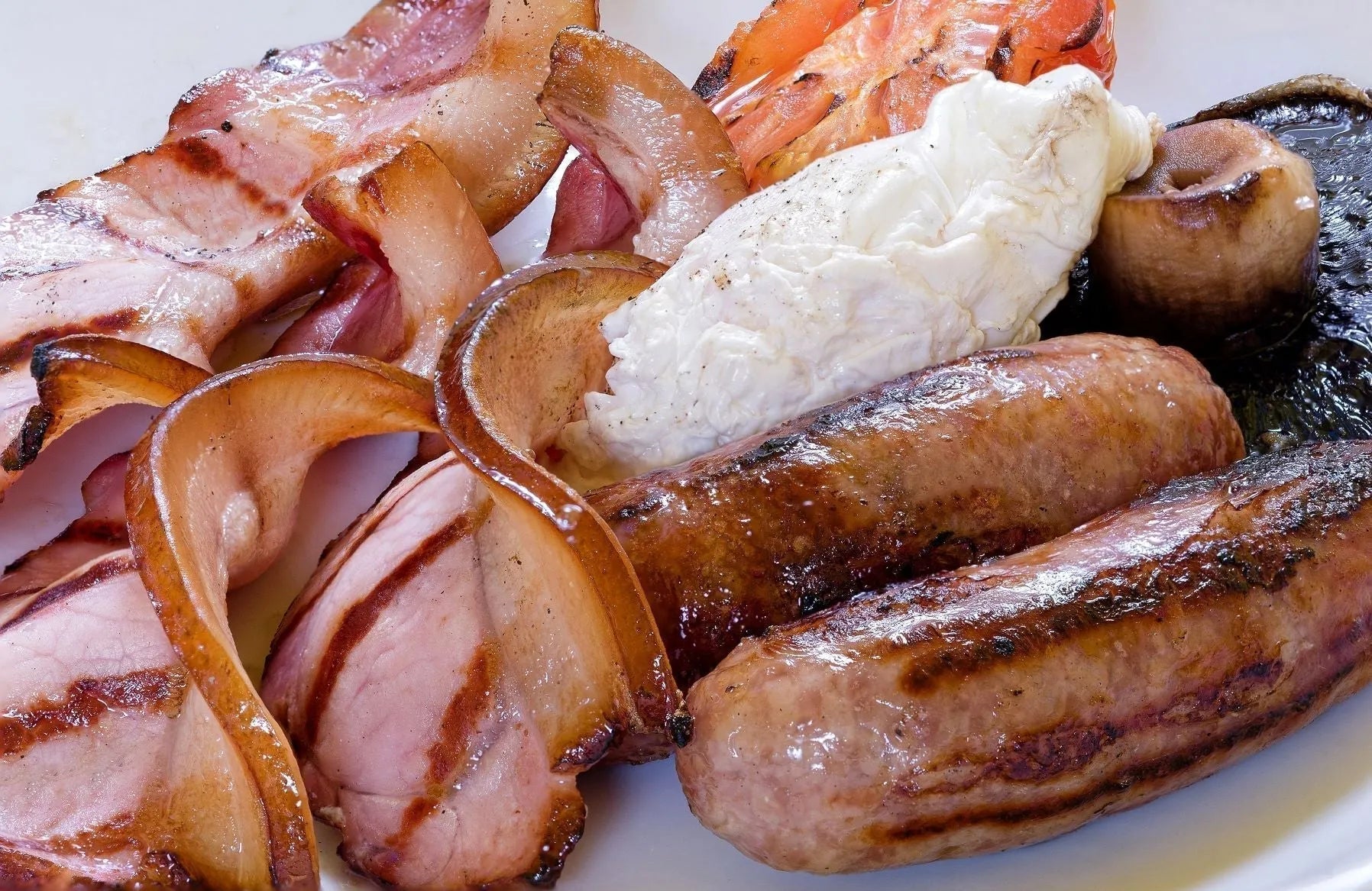 Thin slices of dry-cured smoked streaky bacon from Primrose Herd, displayed on a breakfast plate with eggs and toast.