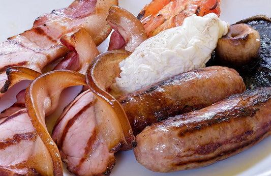Thin slices of dry-cured smoked streaky bacon from Primrose Herd, displayed on a breakfast plate with eggs and toast.