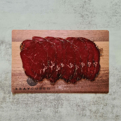 Thinly sliced Bray Cured Classic Bresaola on a charcuterie board with herbs and accompaniments, showcasing premium British beef.