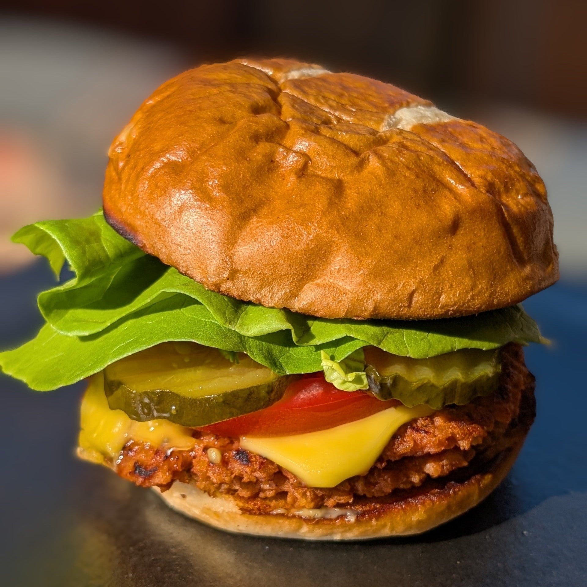 Plant-Based burger with lettuce, tomato, cheese, and pickle on a bun with a blurred background