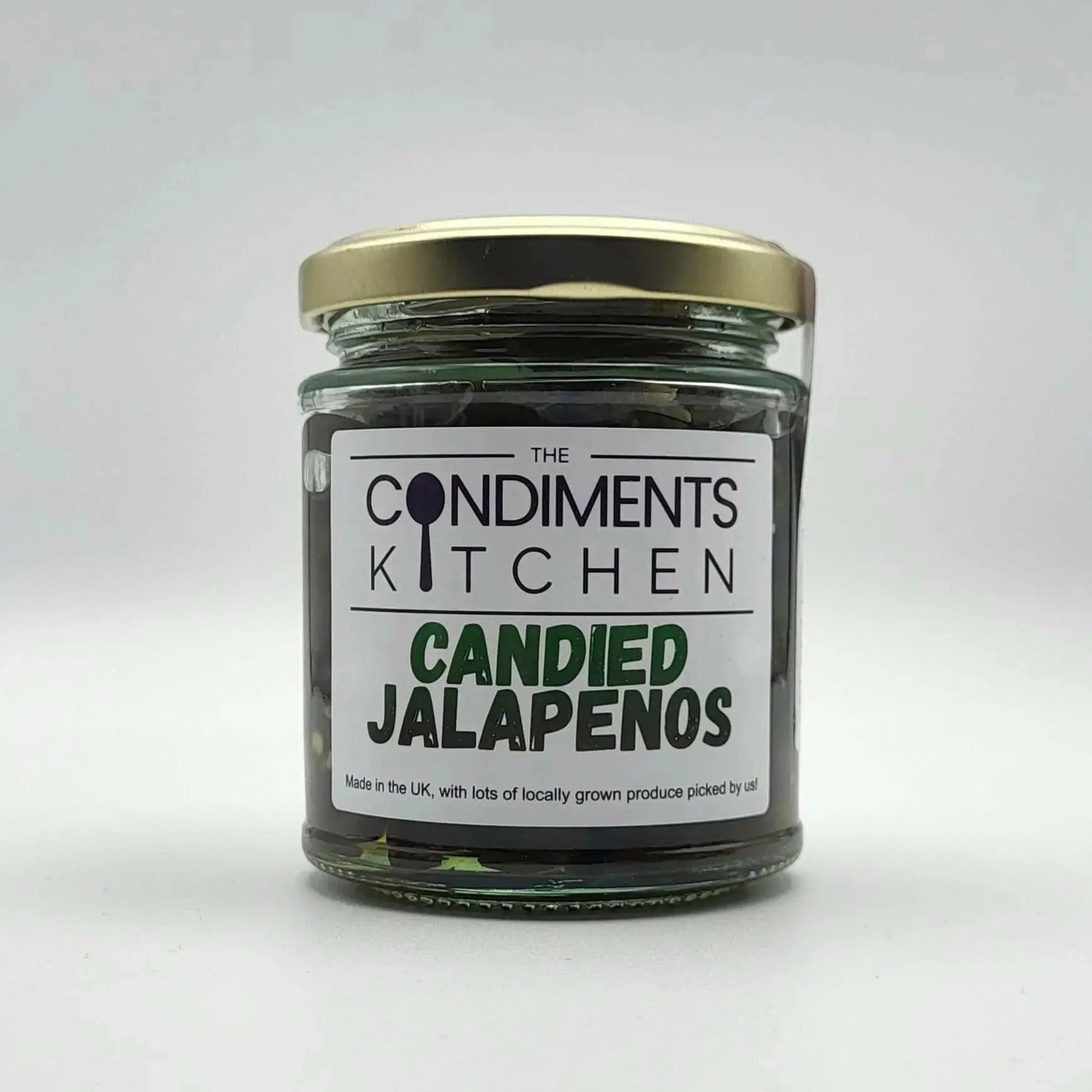 Sweet and spicy candied jalapenos from The Condiments Kitchen shown in a jar with glossy, bright green jalapenos coated in sugary glaze.