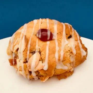 Cherry Bakewell Cookie by Cool Hog Snacks, showing a golden-brown cookie with cherry pieces and almond topping on a white plate.