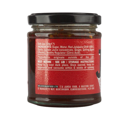 Spicy Janda Chilli Jam jar with red chili peppers and jam spread on a wooden surface, showcasing its vibrant color and texture.