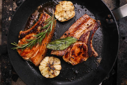 Two beef chops sizzling in a pan, part of the Primrose Herd Family Meat Box, showcasing fresh, cooked meat cuts.