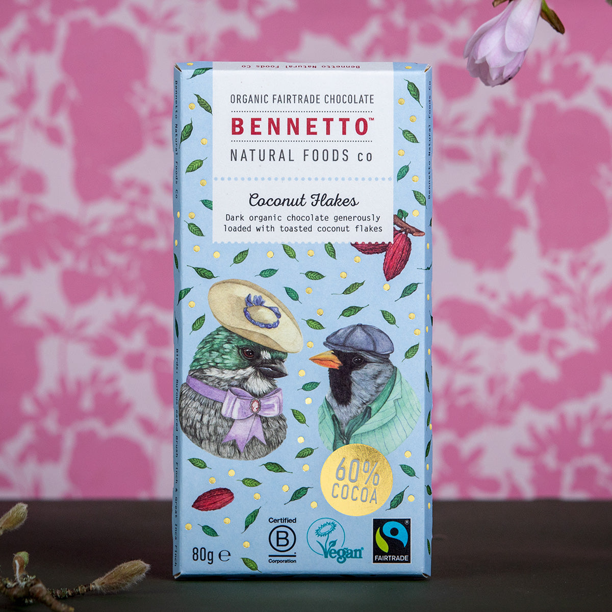 Bennetto Natural Foods UK chocolate coconut flakes in a clear bowl, showing shredded coconut coated with rich chocolate.