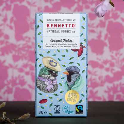Bennetto Natural Foods UK chocolate coconut flakes in a clear bowl, showing shredded coconut coated with rich chocolate.