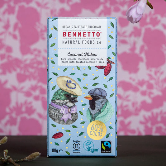 Bennetto Natural Foods UK chocolate coconut flakes in a clear bowl, showing shredded coconut coated with rich chocolate.