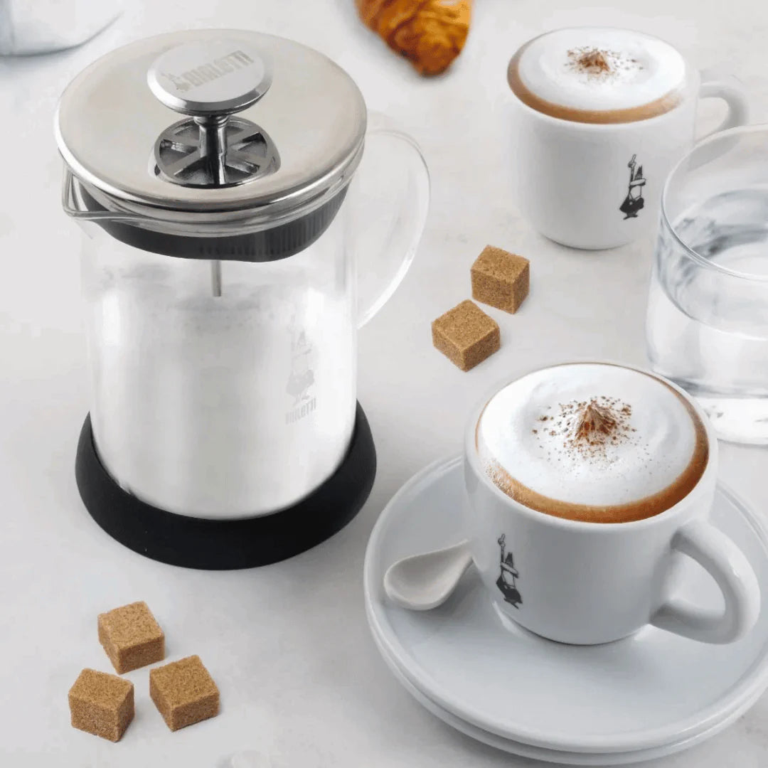 Bialetti Tuttocrema glass milk frother for coffee, with stainless steel handle and clear glass body, used for frothing milk.