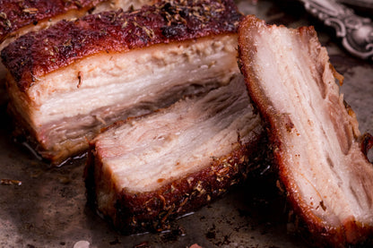 Slices of cooked outdoor-reared Primrose Herd pork belly on the bone, showcasing crispy, golden-brown skin and tender meat.