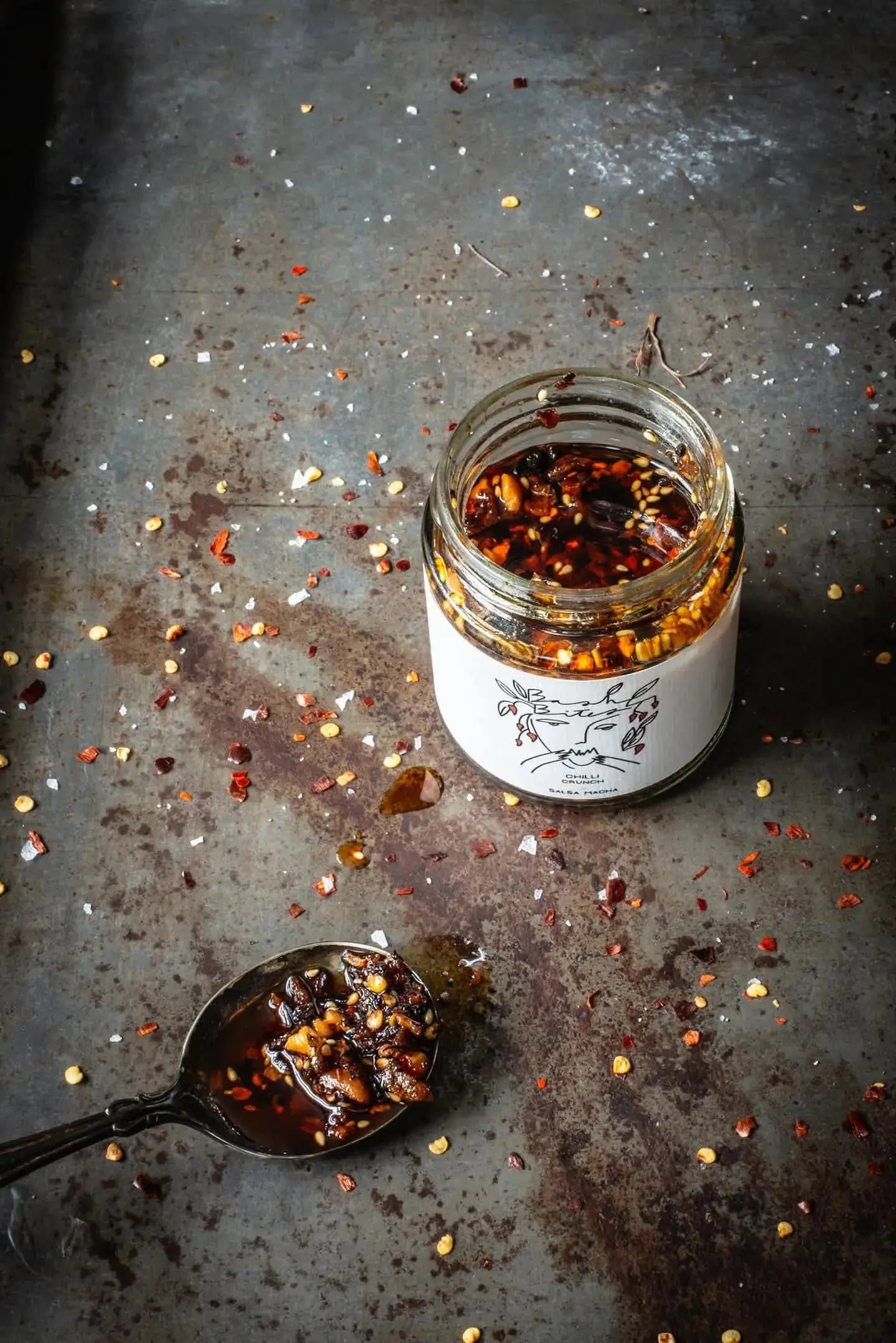 Bashbites Chilli Crunch condiment in a jar, featuring vibrant red chili flakes and crunchy texture, ideal for adding spice to dishes.