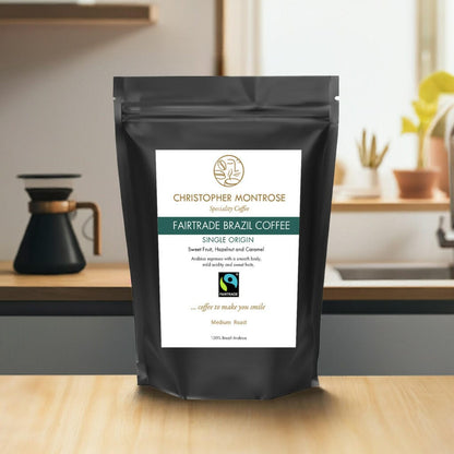 Fairtrade Brazil Arabica coffee beans in a glass jar on a kitchen countertop, with a coffee grinder and cups in the background.