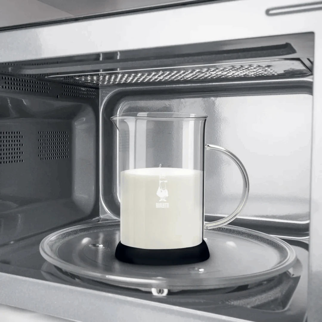 Bialetti Tuttocrema glass milk frother with a clear glass body and stainless steel lid, used for frothing milk.