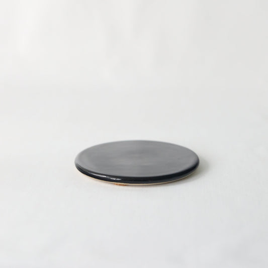 Handmade black ceramic coaster from Katie L Thompson Designs with a smooth, glossy finish and rounded edges.