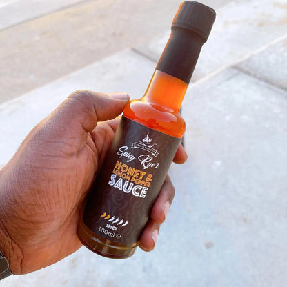 Spicy Ryes Honey & Lemon Pepper Hot Sauce bottle with yellow lemon slices and black peppercorns on a wooden surface.